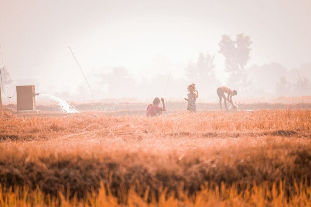 सूखे खेत में पानी के ट्यूबवेल के पास खेलते बच्चे, जो ग्लोबल वार्मिंग के कारण बढ़ते जल संकट और सूखे की स्थिति को दर्शाता है।