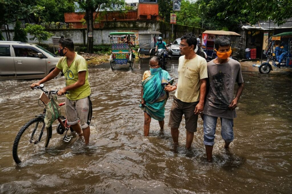 बाढ़ और जलभराव वाली सड़क से गुजरते हुए आम लोग, जो जलवायु परिवर्तन के कारण होने वाले चरम मौसम और शहरी बाढ़ को दर्शाता है।
